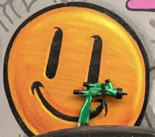 Pistola de pintura híbrida R25 NA Smiley David Vergara colocada sobre una pared con un grafiti de un smiley.